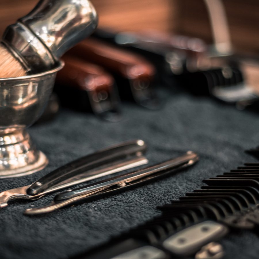 Navalhas, pincel de barba com tigela de metal, pentes e escovas de barbeiro dispostos sobre pano escuro na bancada da barbearia