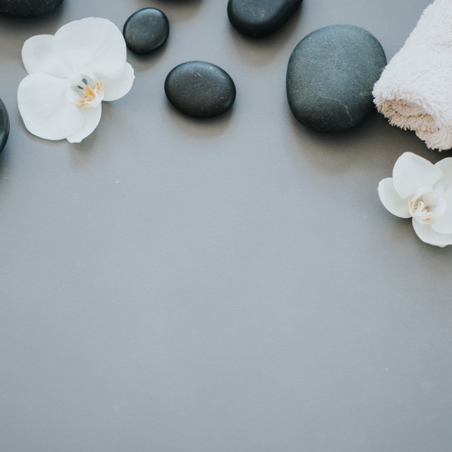 Pedras quentes de massagem, orquídeas brancas e toalha enrolada sobre superfície cinza em ambiente de spa