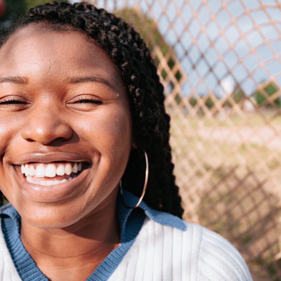 Mulher jovem sorrindo abertamente ao ar livre, em close, com dentes brancos e alinhados bem visíveis sob luz natural