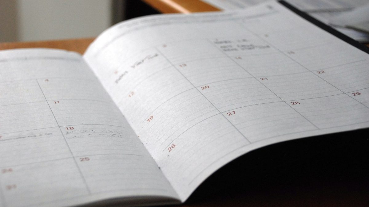 Caderno com calendário de postagens anotado à mão ao lado de celular sobre a mesa