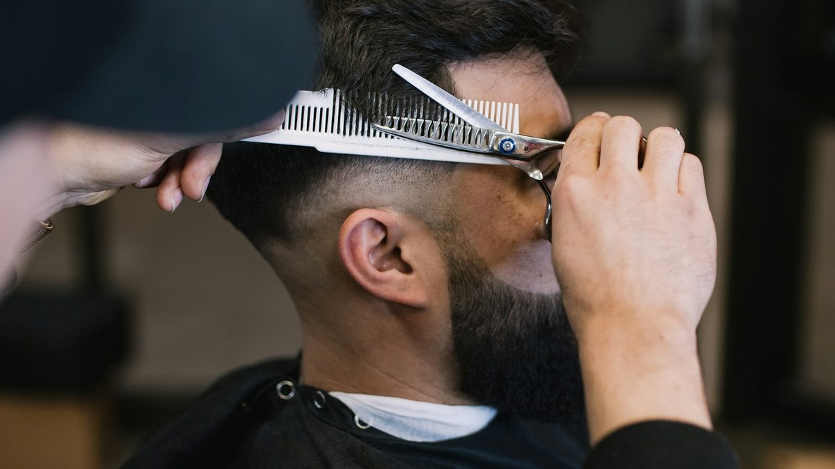 Barbeiro finalizando corte de cabelo masculino em barbearia com cadeira e espelho
